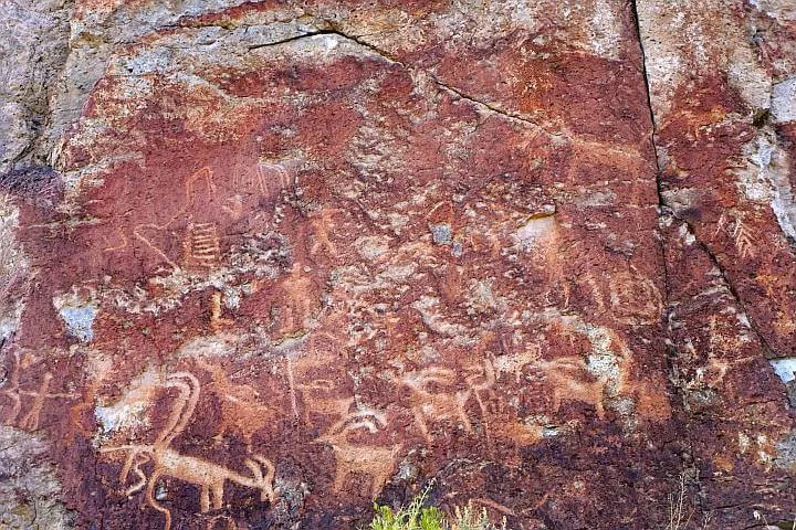 Petroglyphs depicting people and animals, carved into a red rock.