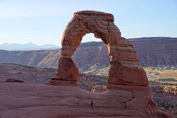 A hiker walking in front of Delicate Arch