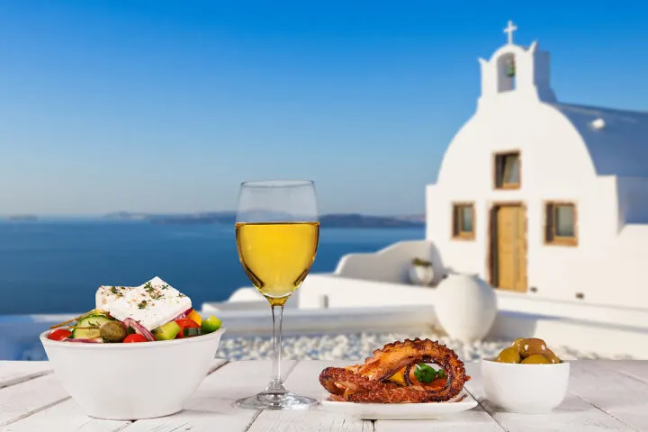 Glass of white wine, olives, octopus, and Greek salad - traditional food of Greece.