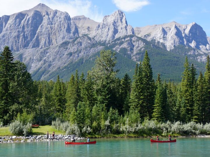 Two red canoes paddling the Bow River in Canmore with mountain backdrop.