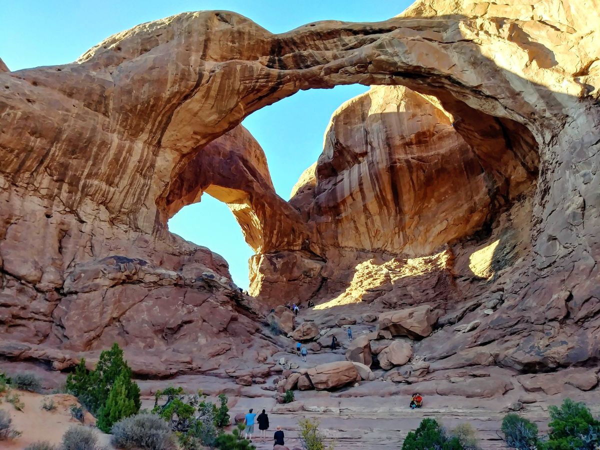 Hikers look tiny under Double Arch at Arches National Park.