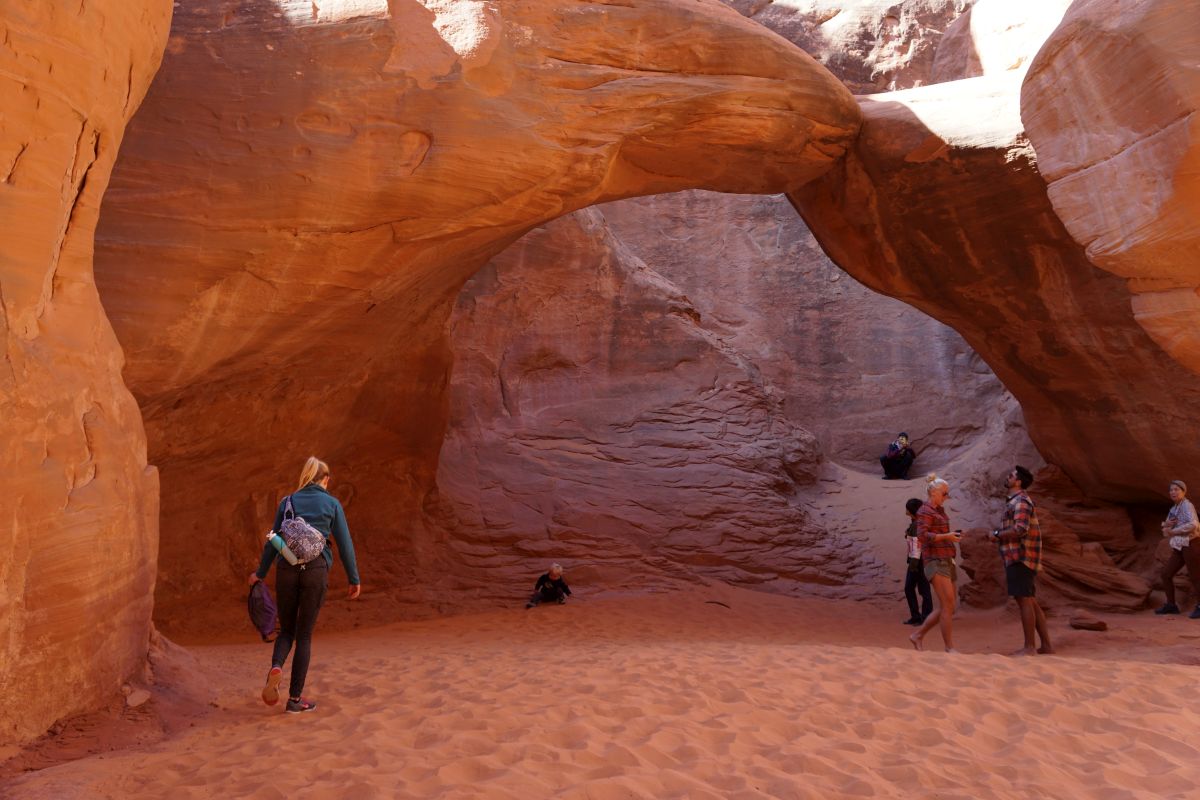 Sand Dune Arch with hikers walking in the sand below the arch.