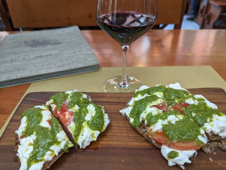 Burrata cheese with pesto and tomato on bread with glass of red wine.