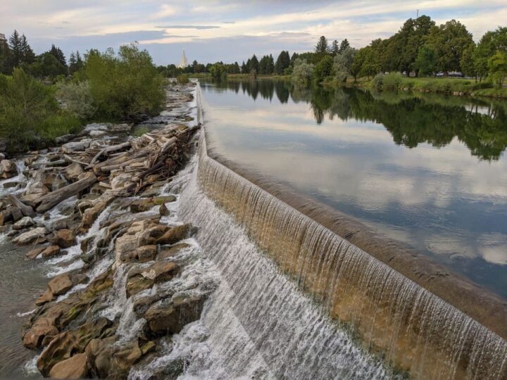 Scenic view of the Snake River waterfall with Idaho Temple in the distance in Idaho Falls, Idaho.