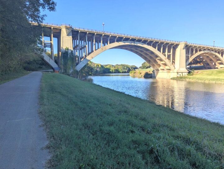 Paved path alongside West Fork Trail Trinity River with bridge in Fort Worth TX.
