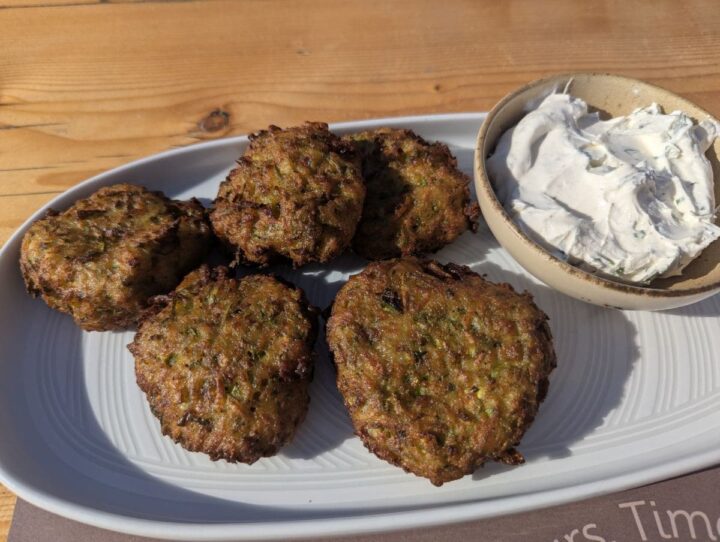 Greek kolokithokeftedes (fried zucchini balls) with tzatziki sauce on a white plate.